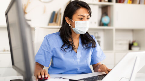 Arzthelferin mit Maske arbeitet am PC