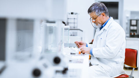 Wissenschaftler sitzt mit Laborkittel am Tisch, vertieft in seine Arbeit.