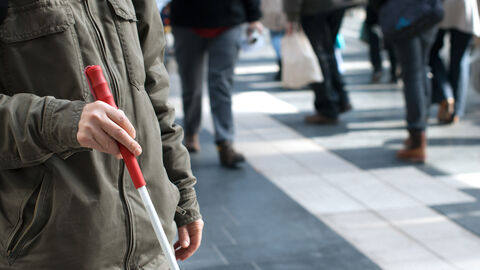 Ein Mann mit Blindenstock vor einer Menge Menschen