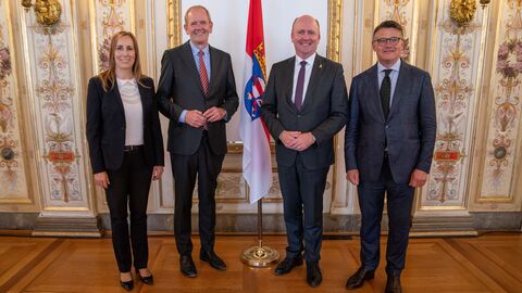 Amtswechsel im Hessischen Rechnungshof Vier Personen stehen zum Gruppenbild aufgestellt vor einer Wand und der Hessen-Flagge.