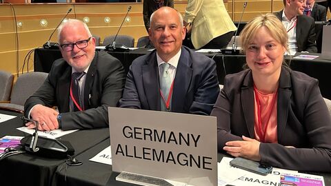 Innenminister Roman Poseck mit den Bundestagsabgeordneten Marja-Liisa Völlers und Wolfgang Hellmich Zwei Männer und eine Frau schauen in Kamera. Auf dem Schreibtisch vor ihnen ist ein Schild mit der Aufschrift "GERMANY ALLEMAGNE"