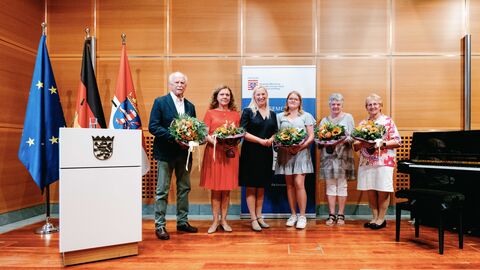 (v.l.n.r.): Eckhard Wolfgang Viehöver (Rheingau-Taunus-Kreis), Piroska Marta Ritter (Frankfurt am Main), Gesundheitsministerin Diana Stolz, Lilli Leandra Blumann (Landkreis Bergstraße), Alinda Elisabeth Bauer (Main-Kinzig-Kreis), Dorothea Magdalena Bäcker (Landkreis Limburg-Weilburg). Sechs Personen stehen nebeneinander in einem Raum und halten jeweils einen Blumenstrauß in der Hand.